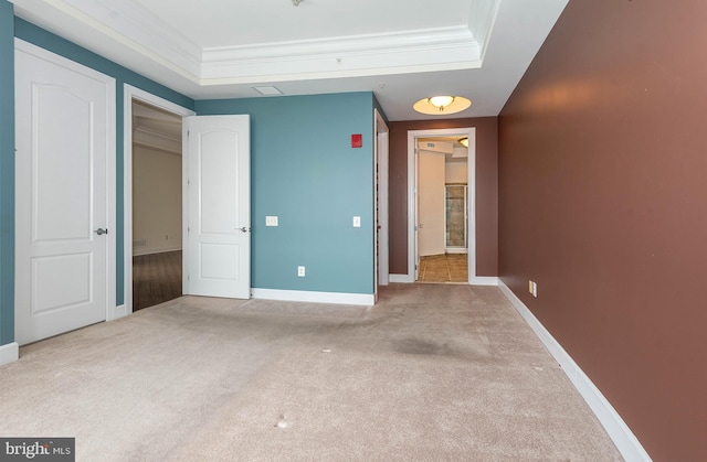 unfurnished bedroom with a tray ceiling, light carpet, and ornamental molding