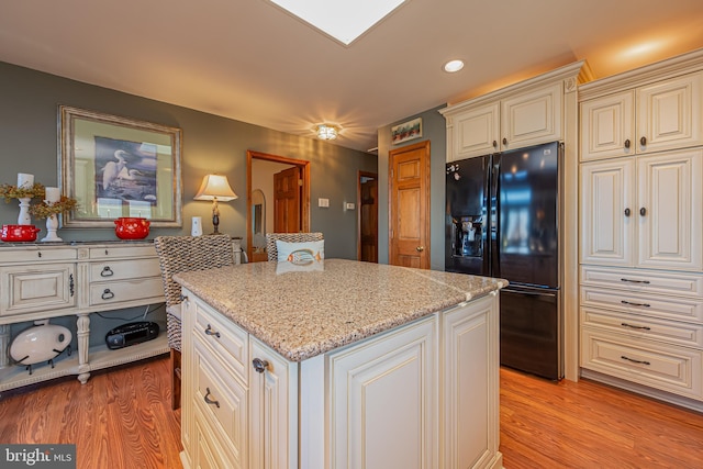 kitchen with a kitchen island, black fridge with ice dispenser, light stone countertops, and light wood-type flooring