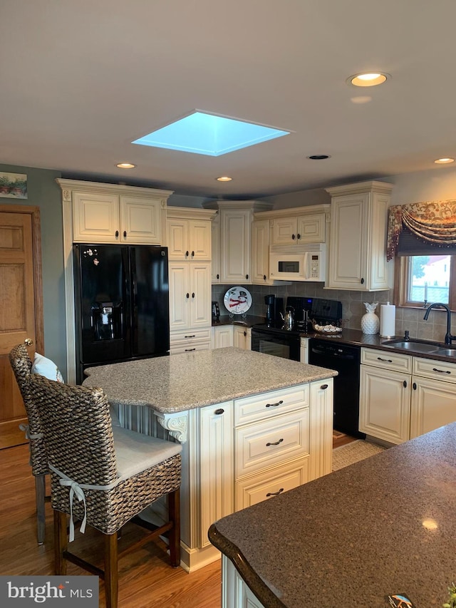 kitchen featuring tasteful backsplash, black appliances, sink, and light wood-type flooring