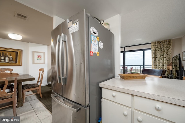 kitchen with light tile floors, white cabinets, and stainless steel refrigerator