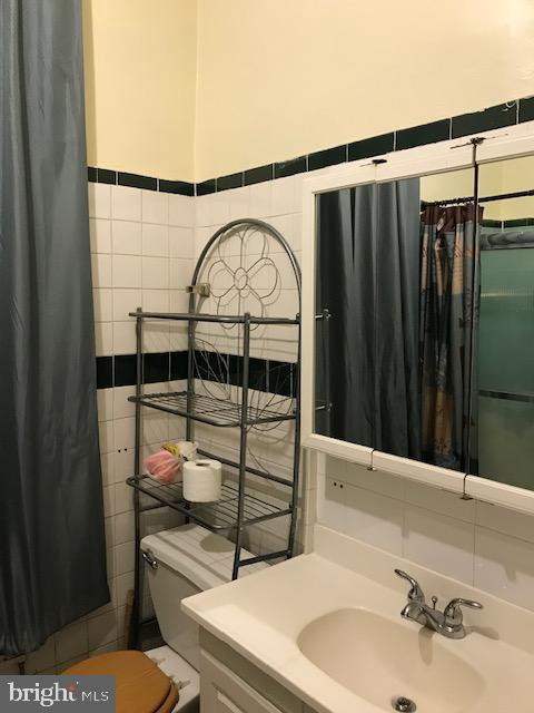 bathroom featuring toilet, vanity, and tile walls