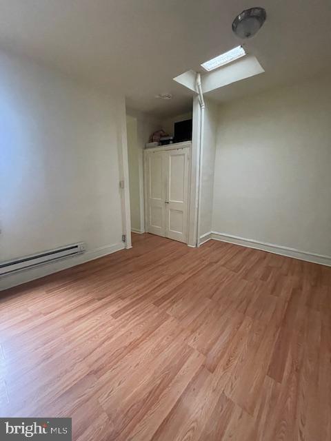 empty room with a skylight, light hardwood / wood-style floors, and baseboard heating