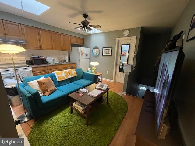 living room with a skylight, ceiling fan, and light wood-type flooring