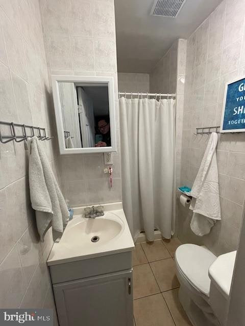 bathroom with vanity with extensive cabinet space, toilet, and tile walls