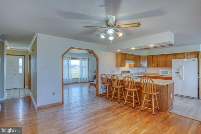 kitchen featuring kitchen peninsula, a breakfast bar area, ceiling fan, light hardwood / wood-style floors, and white appliances