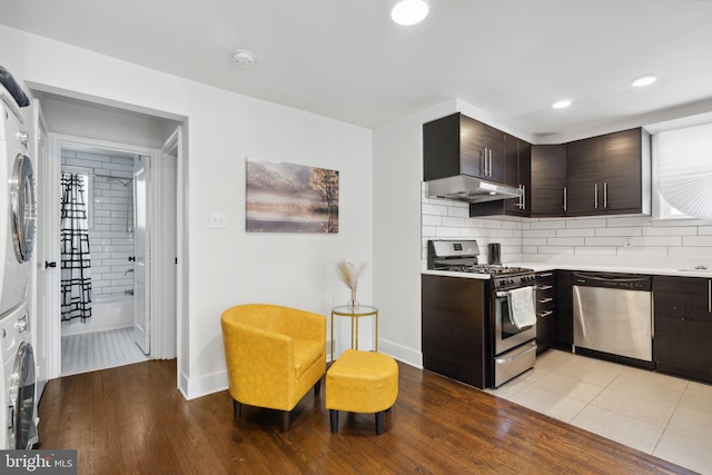 kitchen with appliances with stainless steel finishes, light hardwood / wood-style floors, backsplash, stacked washing maching and dryer, and dark brown cabinets