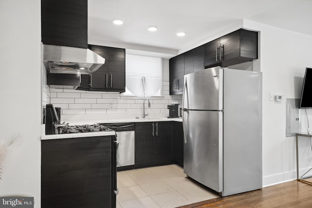 kitchen with wall chimney exhaust hood, backsplash, appliances with stainless steel finishes, sink, and light tile floors