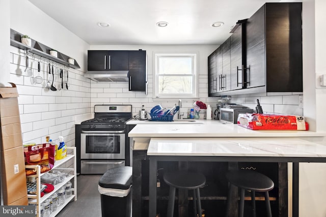 kitchen featuring a breakfast bar, stainless steel gas range oven, kitchen peninsula, extractor fan, and tasteful backsplash