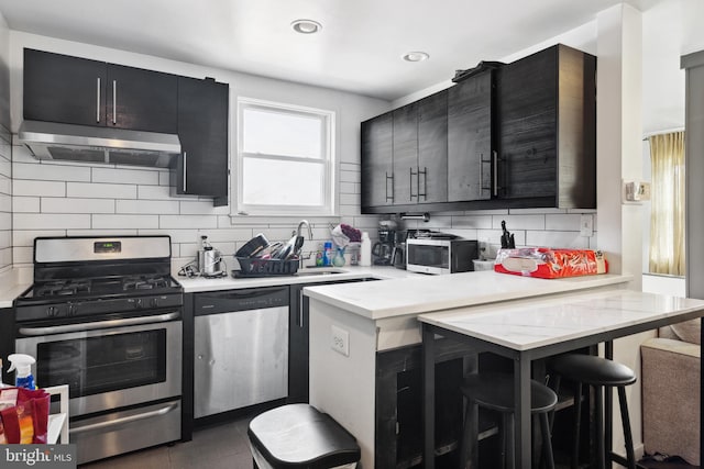 kitchen featuring kitchen peninsula, stainless steel appliances, tasteful backsplash, a kitchen breakfast bar, and dark tile floors