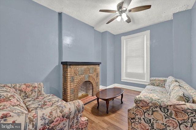 living area featuring a brick fireplace, a textured ceiling, ceiling fan, and light wood-type flooring