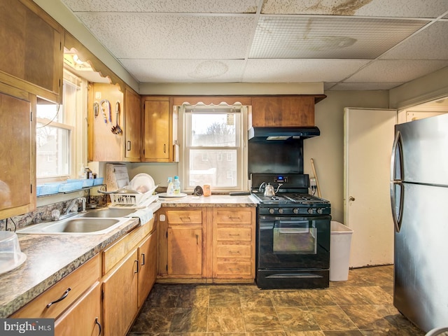 kitchen with black range with gas stovetop, stainless steel fridge, dark tile floors, and a drop ceiling