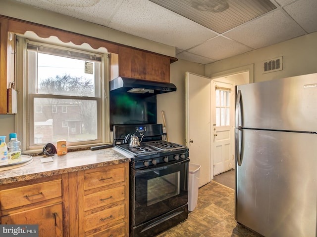 kitchen with wall chimney exhaust hood, stainless steel fridge, black gas range, and a paneled ceiling