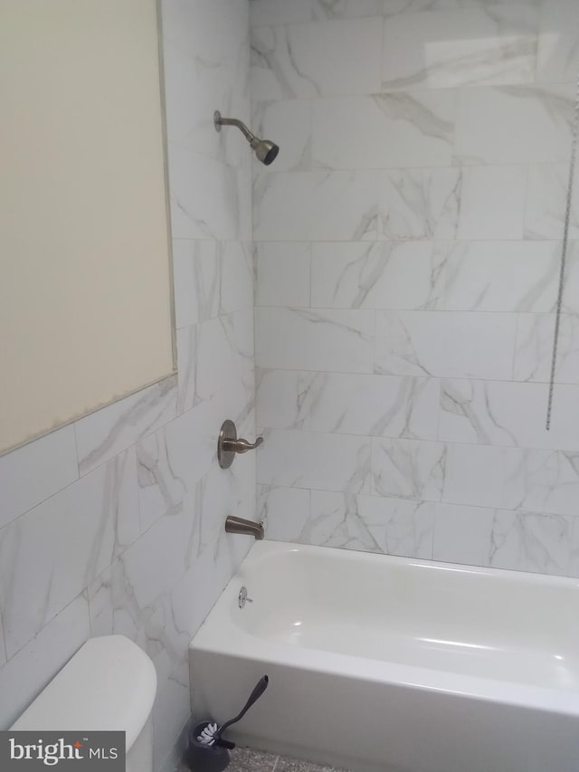 bathroom with tile walls, toilet, and tiled shower / bath