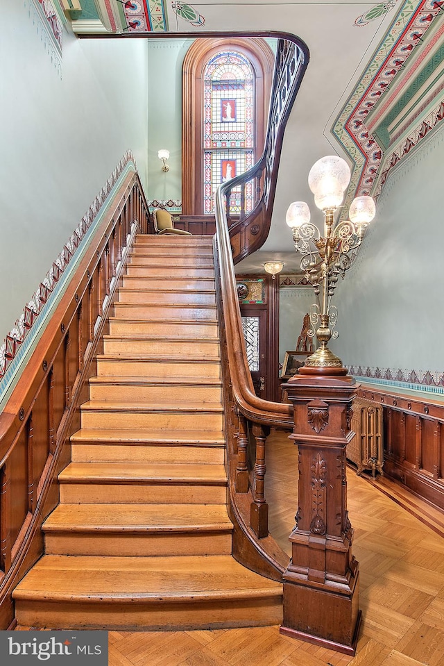 staircase with light parquet floors and an inviting chandelier