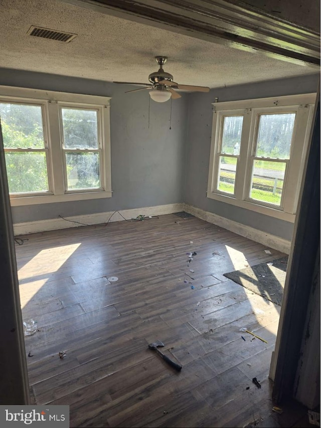 unfurnished room with ceiling fan, a healthy amount of sunlight, dark hardwood / wood-style floors, and a textured ceiling