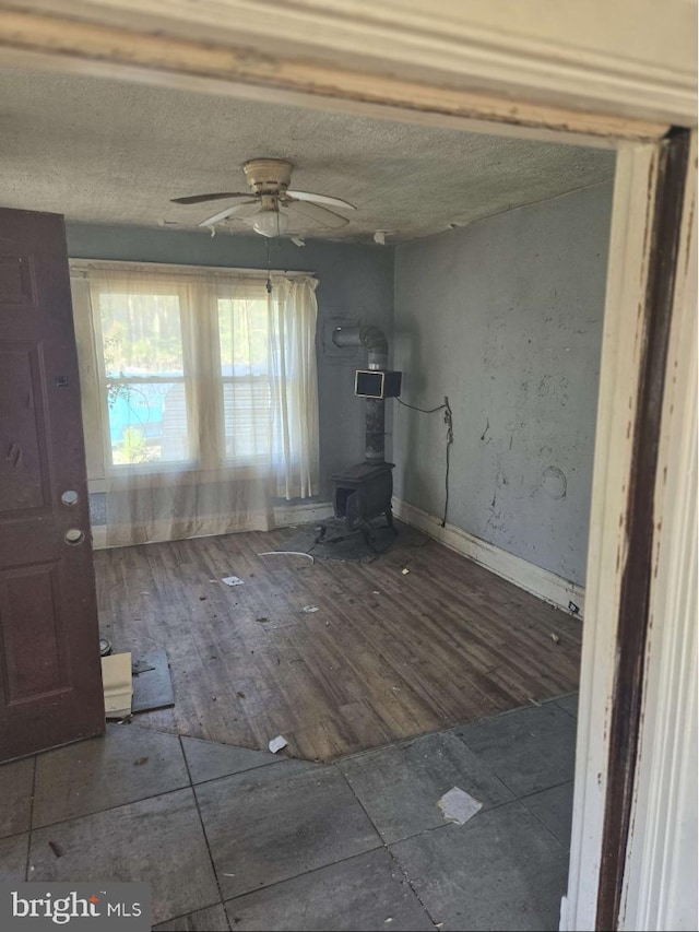 unfurnished living room featuring a wood stove, ceiling fan, and dark wood-type flooring