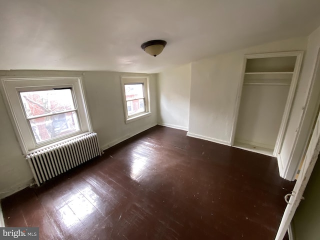 unfurnished bedroom featuring a closet, lofted ceiling, radiator heating unit, and dark wood-type flooring