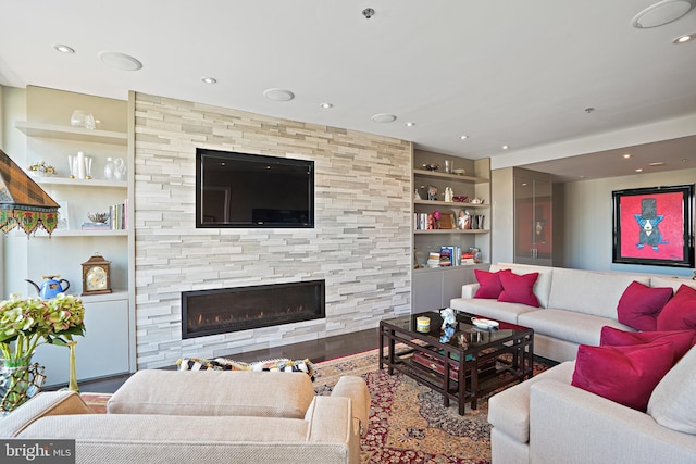 living room featuring hardwood / wood-style floors, built in shelves, and a stone fireplace