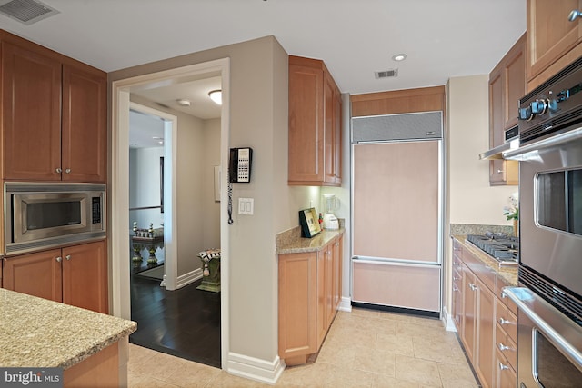 kitchen with light hardwood / wood-style floors, light stone counters, and built in appliances