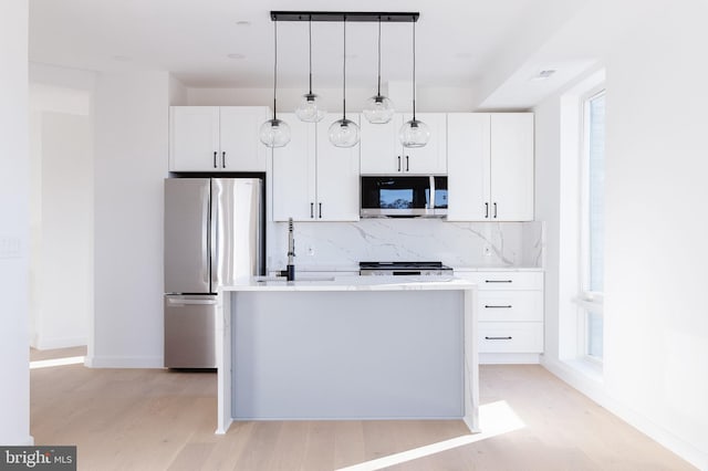 kitchen with an island with sink, hanging light fixtures, appliances with stainless steel finishes, light hardwood / wood-style floors, and white cabinetry