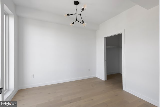 unfurnished bedroom with a closet, a notable chandelier, a walk in closet, and light hardwood / wood-style flooring