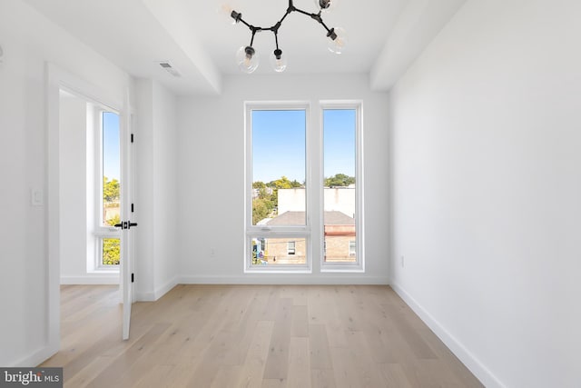 spare room featuring a chandelier and light hardwood / wood-style floors