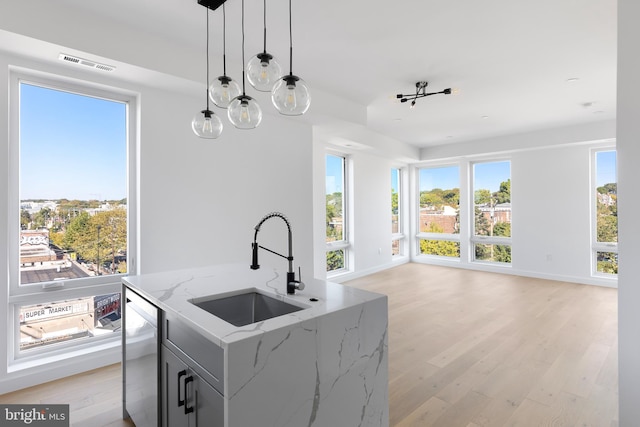 kitchen with pendant lighting, stainless steel dishwasher, light hardwood / wood-style floors, light stone countertops, and a center island with sink