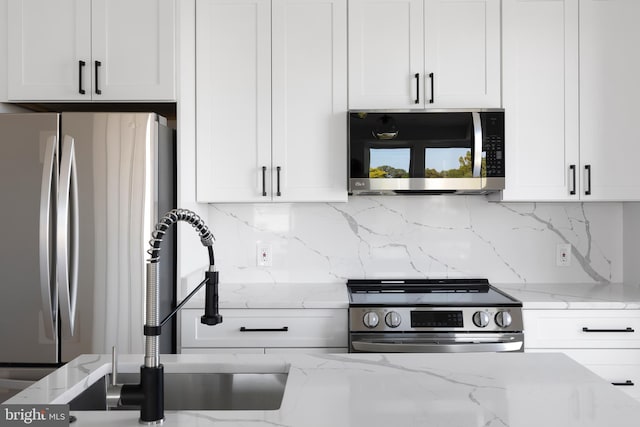 kitchen featuring white cabinets, light stone countertops, backsplash, and stainless steel appliances