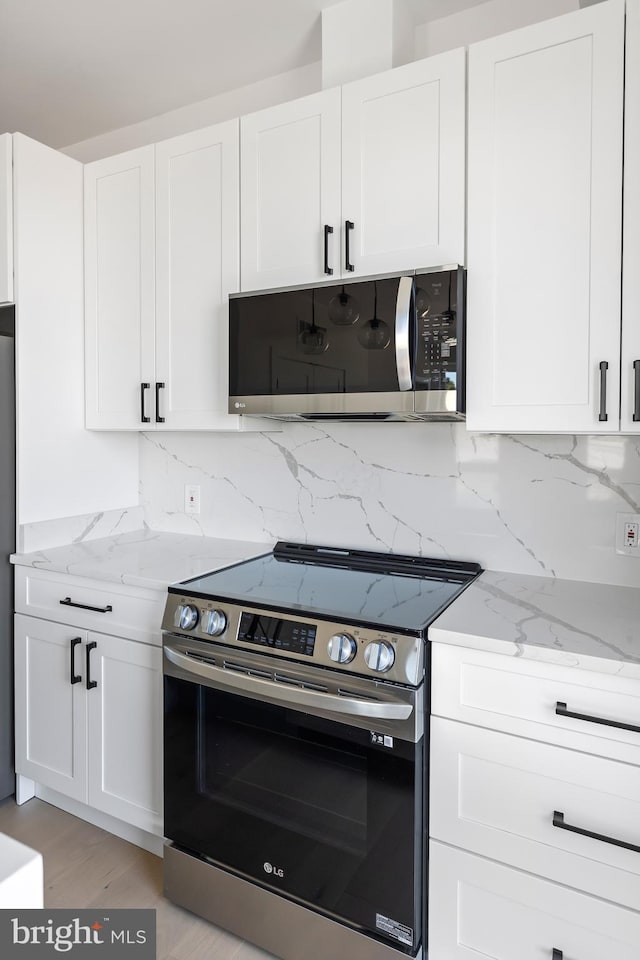 kitchen with white cabinetry, light wood-type flooring, stainless steel appliances, and light stone countertops