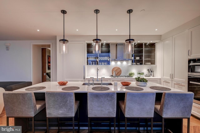 kitchen with white cabinets, backsplash, a kitchen island with sink, and wall chimney exhaust hood