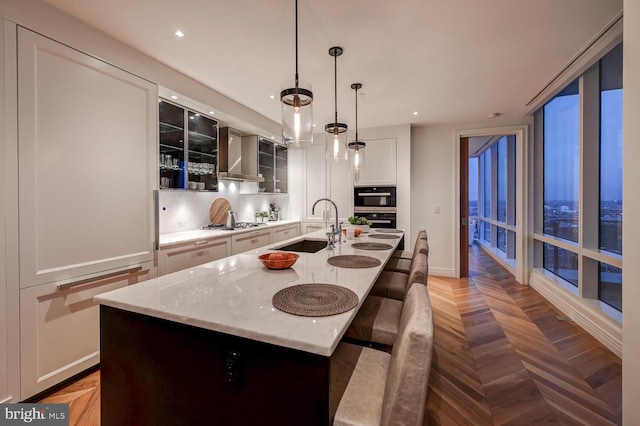 kitchen featuring light parquet floors, a breakfast bar, wall chimney exhaust hood, hanging light fixtures, and a kitchen island with sink