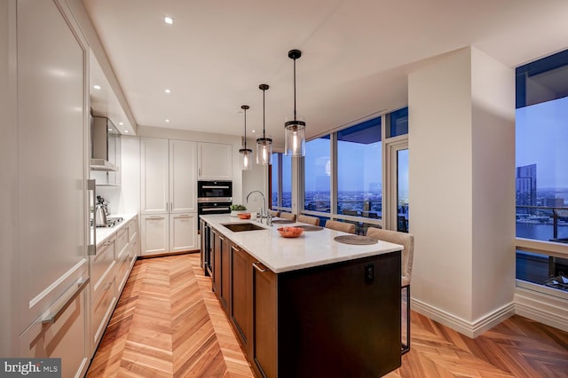 kitchen with decorative light fixtures, light parquet floors, white cabinetry, a center island with sink, and sink