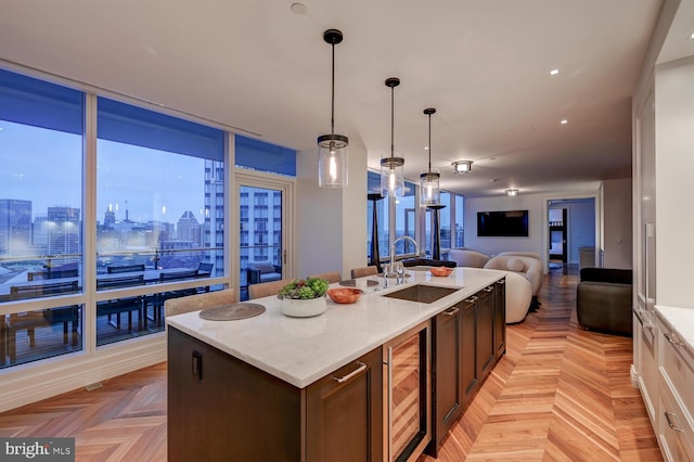 kitchen with decorative light fixtures, sink, wine cooler, a center island with sink, and light parquet flooring