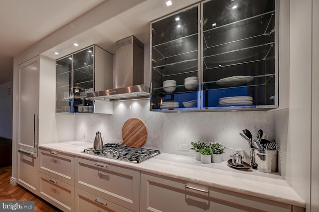 kitchen with gray cabinets, stainless steel gas cooktop, backsplash, light stone countertops, and wall chimney range hood