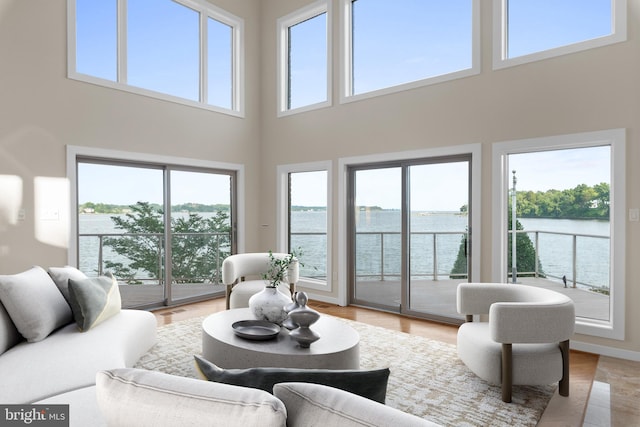 living room with a water view, light hardwood / wood-style flooring, and a towering ceiling