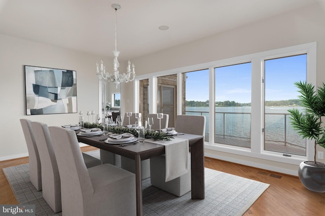 dining area with an inviting chandelier, a water view, and light hardwood / wood-style floors