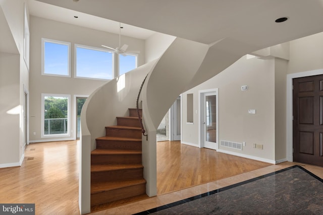 staircase featuring light hardwood / wood-style floors, ceiling fan, and a towering ceiling