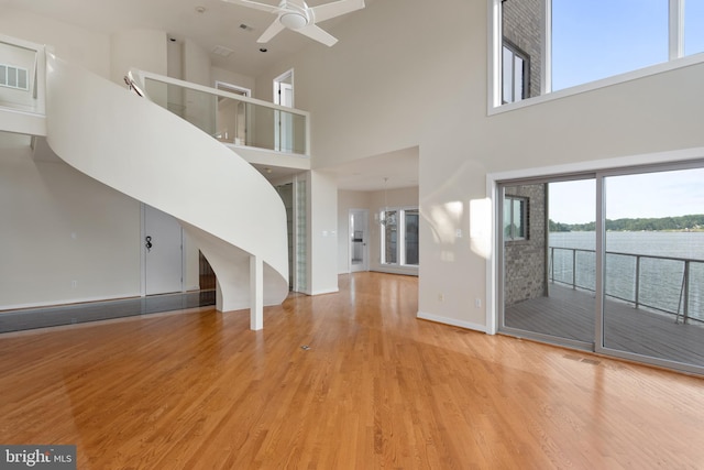 unfurnished living room with a high ceiling, ceiling fan with notable chandelier, a healthy amount of sunlight, and light wood-type flooring