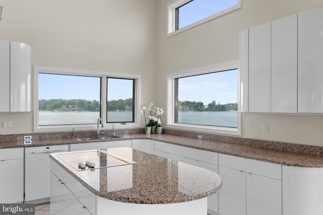 kitchen featuring white cabinetry, dark stone countertops, a water view, sink, and white dishwasher