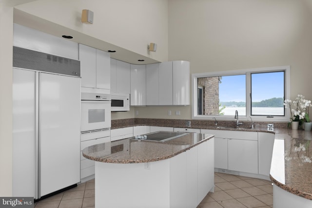 kitchen featuring white appliances, sink, light tile floors, a towering ceiling, and white cabinets