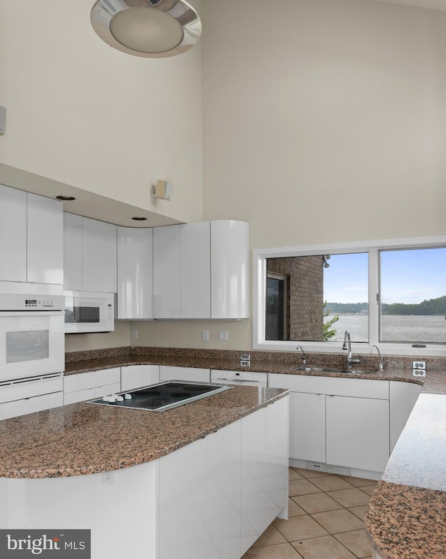 kitchen featuring light tile floors, dark stone counters, white appliances, white cabinets, and sink