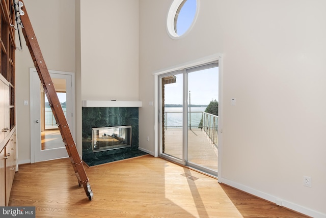 unfurnished living room with a towering ceiling, a premium fireplace, and light wood-type flooring