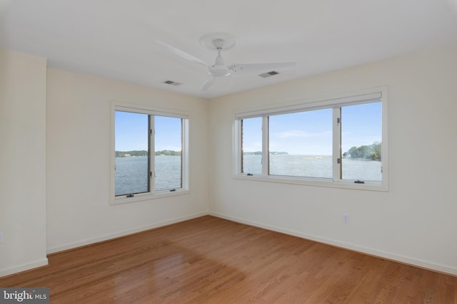 spare room with light hardwood / wood-style floors, ceiling fan, and a water view