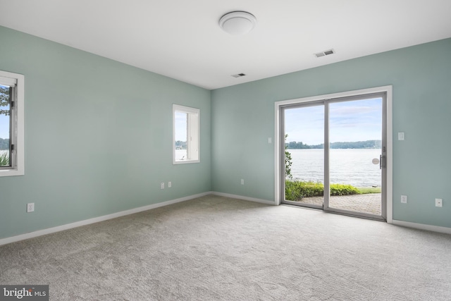 unfurnished room featuring a water view and light colored carpet