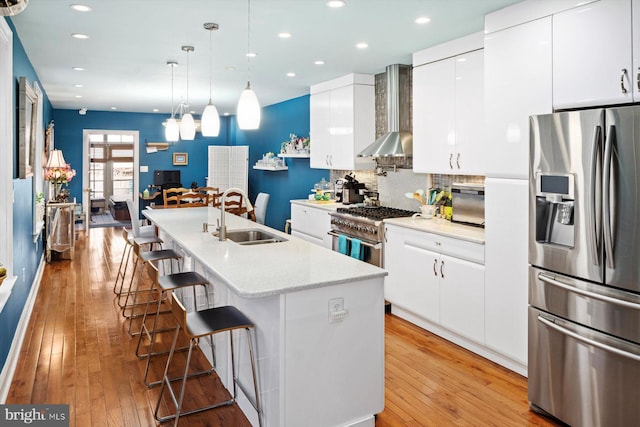 kitchen featuring appliances with stainless steel finishes, pendant lighting, light hardwood / wood-style floors, sink, and wall chimney exhaust hood