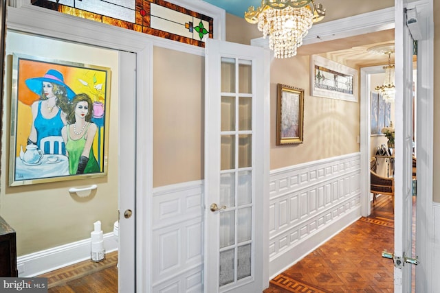 hallway with french doors, dark parquet floors, ornamental molding, and a chandelier