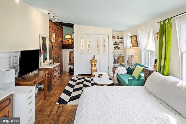 bedroom with a closet, rail lighting, dark hardwood / wood-style floors, and brick wall