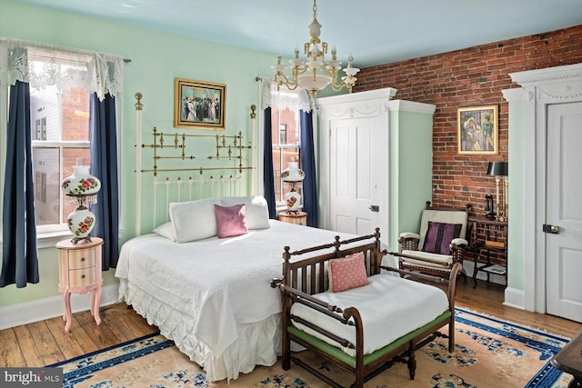 bedroom with a notable chandelier, brick wall, and light wood-type flooring