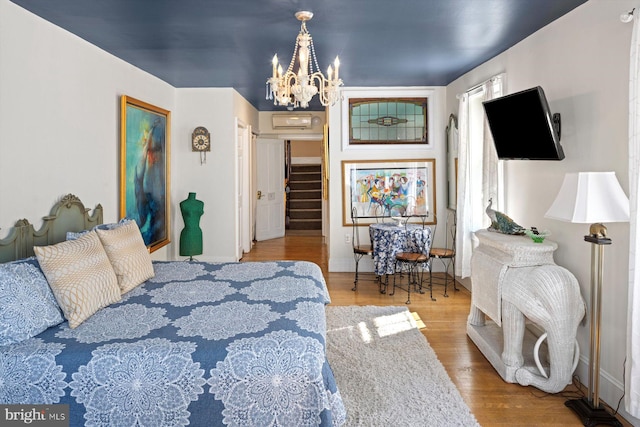 bedroom with a chandelier, light wood-type flooring, and a wall mounted air conditioner