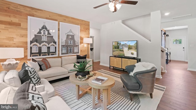 living room with plenty of natural light, ceiling fan, dark wood-type flooring, and wood walls